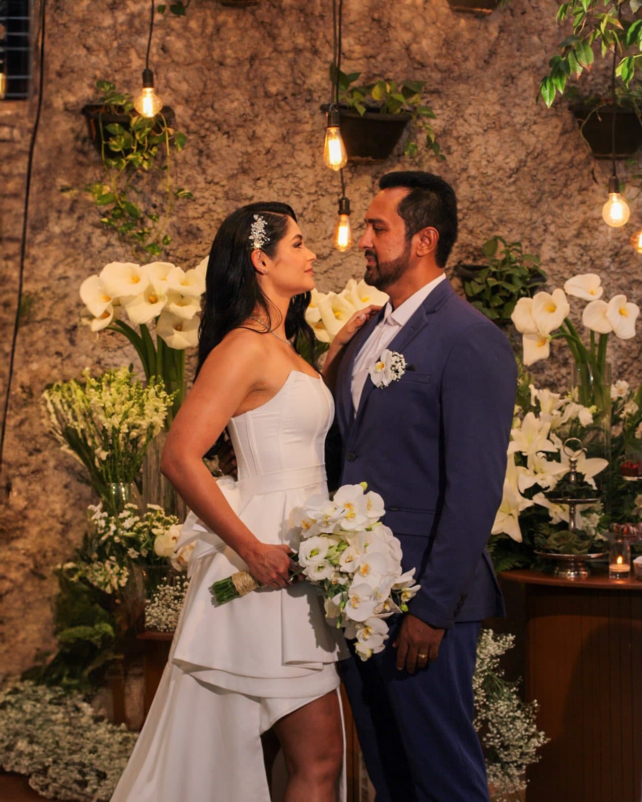 Casal de noivos entre flores brancas na parede de pedra