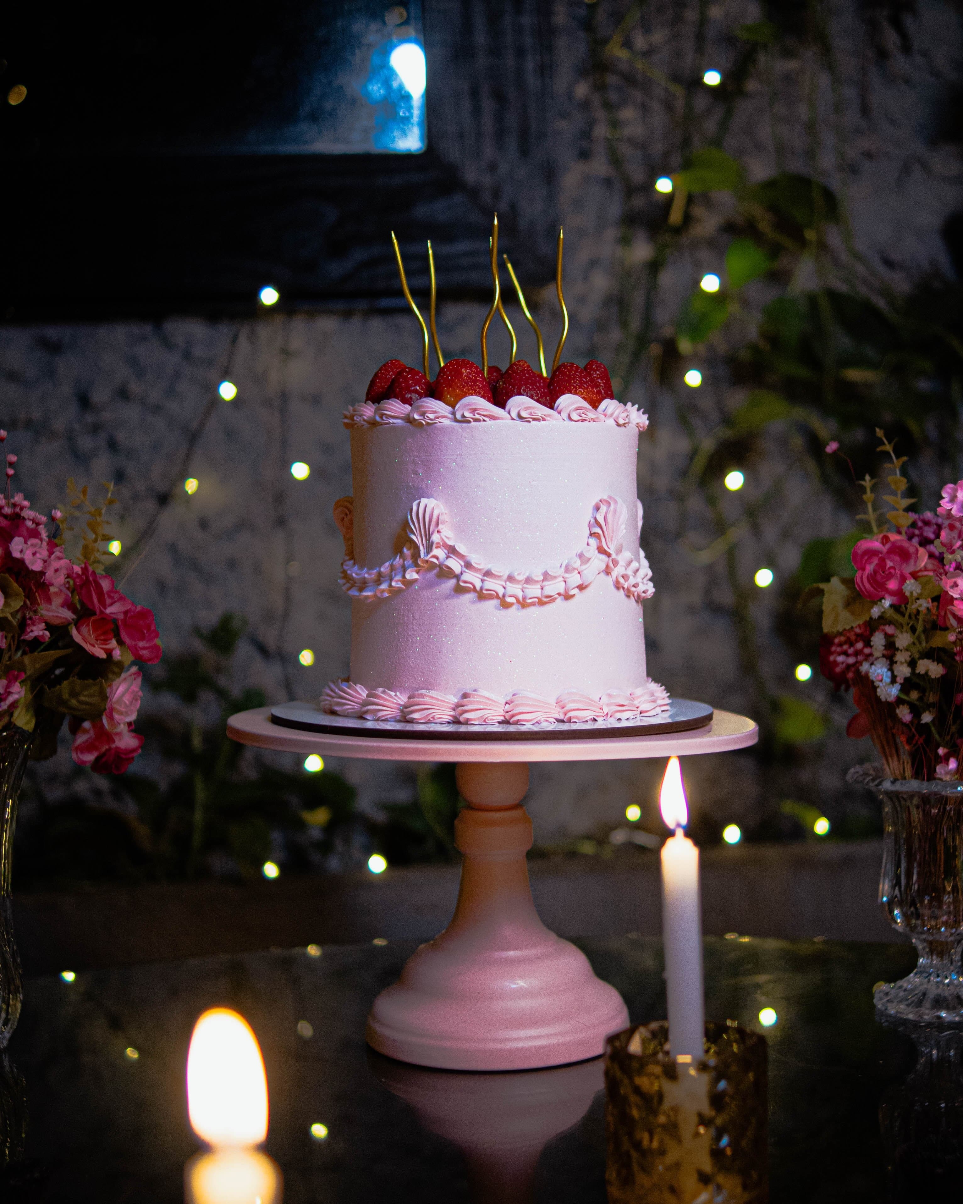 Bolo de aniversário rosa com cerejas, à luz de vela